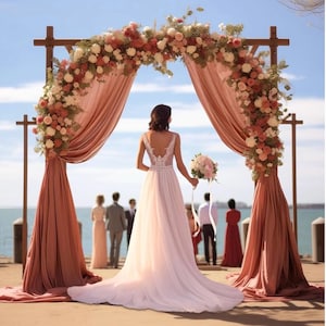 May include: A bride in a white wedding dress with a long train stands under a wooden arch decorated with flowers and draped with peach fabric. A bouquet of flowers is held in her hand. Guests stand in the background.