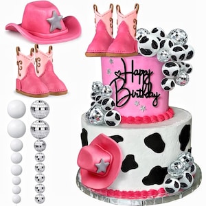 以下が含まれることがあります： 牛柄、ピンクの カウボーイブーツ、ピンクの カウボーイハットで飾られた、ピンクと白の2段の誕生日ケーキ。ケーキはピンクのフロスティングと「ハッピーバースデー」の文字で飾られています。