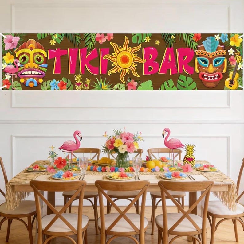 May include: A festive Tiki Bar banner with the words "TIKI BAR" in pink letters, surrounded by tropical flowers, leaves, and tiki masks. A dining table is set with flamingo decorations, floral centerpieces, and colorful plates.