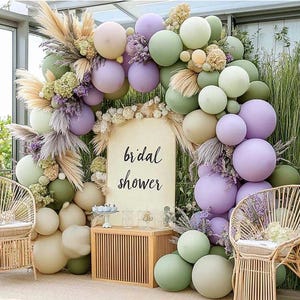 May include: A bridal shower backdrop with a sign that says "bridal shower" surrounded by a garland of lavender, sage green, and cream balloons.