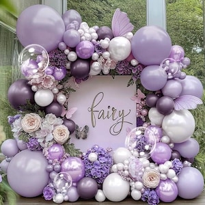 May include: A decorative balloon arch in shades of purple, white, and clear, with the word "fairy" in gold script. The arch is adorned with flowers and butterfly accents, creating a whimsical and festive display.