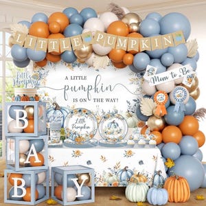Könnte beinhalten: Eine Babyparty-Dekoration mit einem Ballonbogen in Blau, Orange und Gold, einem LITTLE PUMPKIN-Banner, einem Hintergrund mit dem Text A LITTLE PUMPKIN IS ON THE WAY, gestapelten Boxen mit der Aufschrift BABY und Tischdeko mit Kürbismotiven.