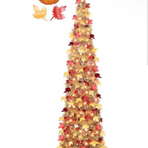 Puede incluir: Un árbol de oropel dorado, alto y delgado, decorado con luces blancas cálidas y hojas de arce de colores otoñales en tonos rojos, naranjas y amarillos. Una pequeña calabaza decorativa se sitúa en la parte superior de la estructura.