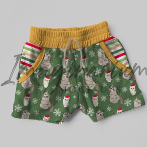 May include: Green shorts with a Christmas cat pattern. The shorts have a yellow waistband and striped pockets.