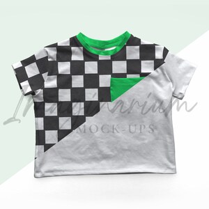 May include: White t-shirt with a black and white checkered pattern on the left side and a green pocket. The neckline and sleeve cuffs are trimmed with green. The shirt is a mock-up.