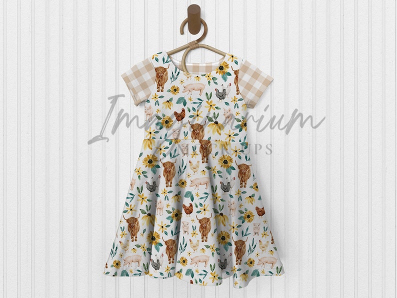 K&ouml;nnte beinhalten: Ein wei&szlig;es Kleid mit einem braunen, gelben und gr&uuml;nen Farmtier-Druck. Das Kleid hat kurze &Auml;rmel mit einem karierten Muster und einen Volant-Rock.