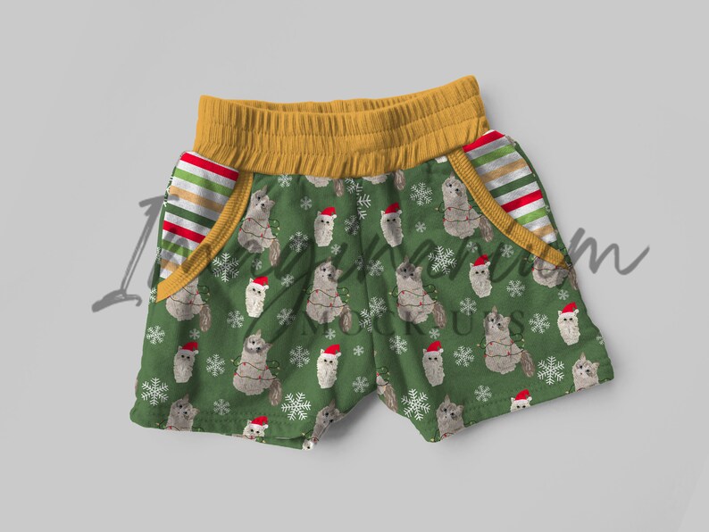 May include: Green shorts with a Christmas cat pattern. The shorts have a yellow waistband and red and white striped pockets.