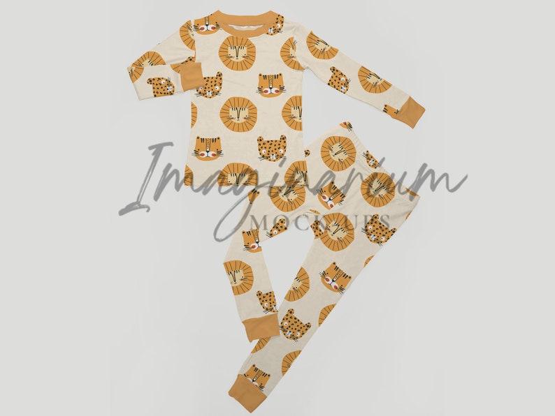 May include: A set of pajamas for children featuring a cream background with a repeating pattern of orange lion faces. The pajamas include a long-sleeved shirt and matching pants.