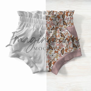 May include: Baby shorts with a high waist and pockets. One side is solid white, the other features a butterfly print in shades of orange, brown, and pink. The shorts have a soft, comfortable appearance.