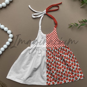 May include: A white halter dress with a red and white gingham pattern and a strawberry print. The dress has a white bodice and a red tie. The dress is designed for a child.
