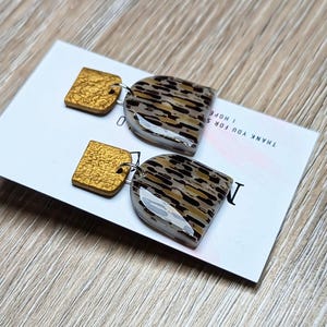 Könnte beinhalten: Ohrringe zum Aufhängen mit einem goldenen Quadrat und einer tropfenförmigen Form mit Leopardenmuster. Die Ohrringe liegen auf einer weißen Karte mit dem Text "THANK YOU FOR SHOPPING. I HOPE".