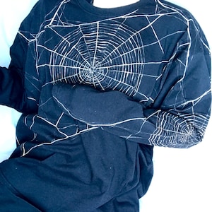 May include: A navy blue long-sleeved shirt with a white spiderweb design. The graphic covers the front and sleeves. The shirt is made of a soft, comfortable material.