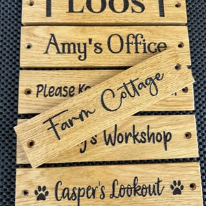 Puede incluir: Cinco letreros de madera con texto negro y una huella de pata. Los letreros dicen: "↑ LOOS ↑", "Amy's Office", "Farm Cottage", "Jo's Workshop", y "Casper's Lookout".