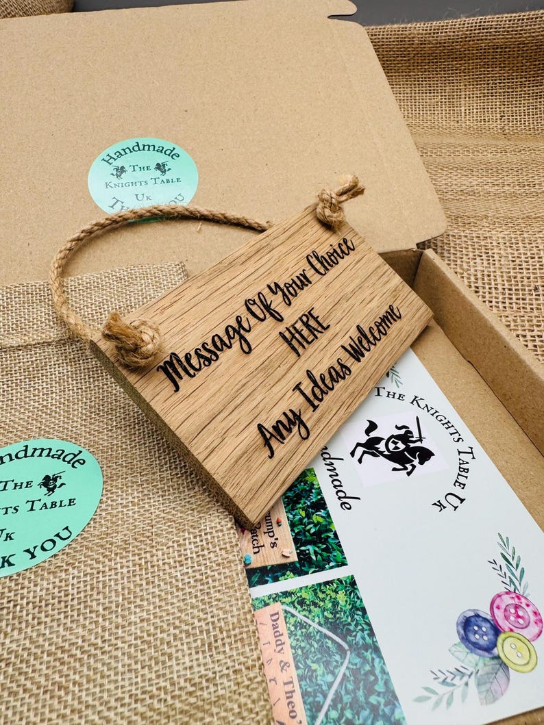 May include: A rectangular wooden sign with the text "Message Of Your Choice HERE Any Ideas Welcome" in black script. The sign is attached to a natural rope and is inside a cardboard box. The box also contains a card with a knight logo.