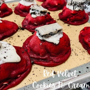 May include: Red velvet cookies topped with white frosting and Oreo cookie pieces. The cookies are arranged on a baking sheet with the text "Seriously Dough" and "Red Velvet Cookies 'n Cream" visible.
