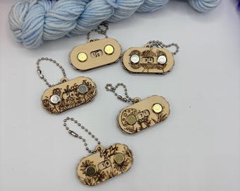 May include: Five oval-shaped wooden row counters with ball chains, each featuring laser-engraved floral, mushroom, or yarn ball designs. These small tools display numerical digits in a central window and include two metallic circular magnets.