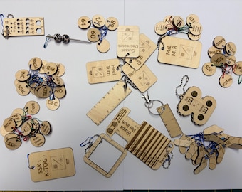 May include: A collection of light-colored wooden knitting tools and stitch markers. The set includes various rectangular tags with engraved text like 'Heel Turn' and 'Gusset Decreases', circular markers with abbreviations, rulers, and a square gauge tool.