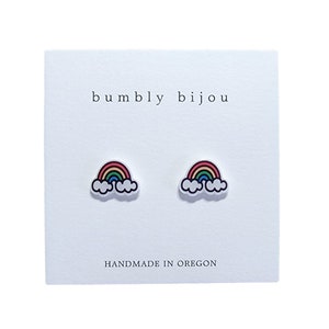 May include: A pair of rainbow and cloud stud earrings on a white card with the text "bumbly bijou" and "HANDMADE IN OREGON".