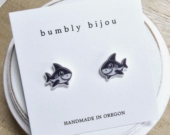 May include: A pair of black and white shark stud earrings on a white card with the text "bumbly bijou" and "HANDMADE IN OREGON".