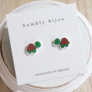 May include: A pair of small, green turtle stud earrings on a white card with the text "bumbly bijou" and "HANDMADE IN OREGON".