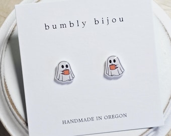Könnte beinhalten: Ohrringe in Geisterform, die jeweils einen kleinen orangefarbenen Becher halten. Sie befinden sich auf einer weißen Karte mit dem Text "bumblly bijou" und "HANDMADE IN OREGON". Ein lustiges, skurriles Accessoire.