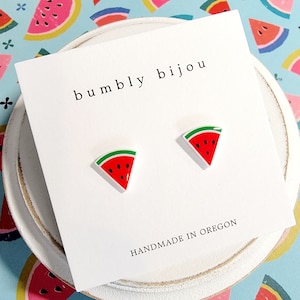 May include: A white card with the text "bumbly bijou" and "HANDMADE IN OREGON" on it. Two small watermelon slice earrings are displayed on the card.