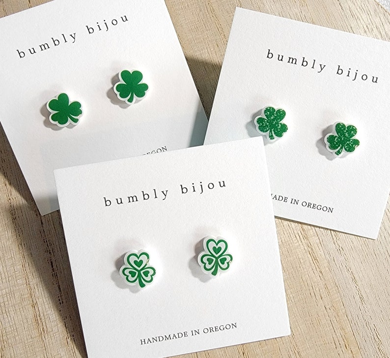 K&ouml;nnte beinhalten: Drei Paare gr&uuml;ne Kleeblatt-Ohrringe auf wei&szlig;en Karten mit dem Text "bumbly bijou" und "handgefertigt in Oregon".
