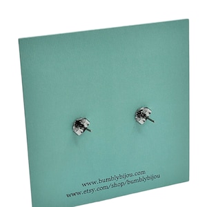 May include: Close-up of two silver-colored earring posts with butterfly backs, displayed on a textured, light teal-colored card. The card has the website address www.bumblbijou.com and the Etsy shop address.
