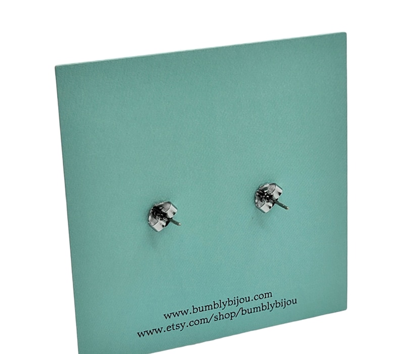 May include: Close-up of two silver-colored earring posts with butterfly backs, displayed on a textured, light teal-colored card. The card has the website address www.bumblbijou.com and the Etsy shop address.