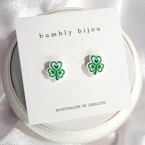 K&ouml;nnte beinhalten: Ein Paar gr&uuml;ne Kleeblatt-Ohrstecker auf einer wei&szlig;en Karte mit dem Text "bumbly bijou" und "HANDMADE IN OREGON".