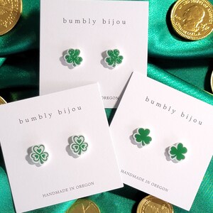 K&ouml;nnte beinhalten: Zwei Paare gr&uuml;ne Kleeblatt-Ohrringe auf wei&szlig;en Karten mit dem Text "bumbly bijou" und "HANDMADE IN OREGON".