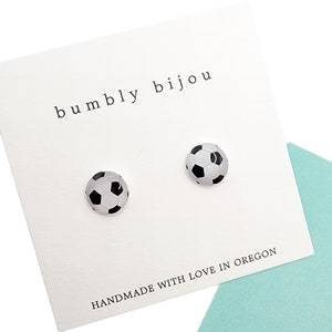 May include: A pair of white and black soccer ball stud earrings on a white card with the text "bumbly bijou" and "HANDMADE WITH LOVE IN OREGON".