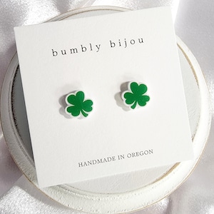 K&ouml;nnte beinhalten: Ein Paar gr&uuml;ne Kleeblatt-Ohrstecker auf einer wei&szlig;en Karte mit dem Text "bumbly bijou" und "HANDMADE IN OREGON".