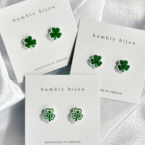 K&ouml;nnte beinhalten: Drei Paar gr&uuml;ne Kleeblatt-Ohrstecker auf wei&szlig;en Karten mit dem Text "bumbly bijou" und "handgefertigt in Oregon".