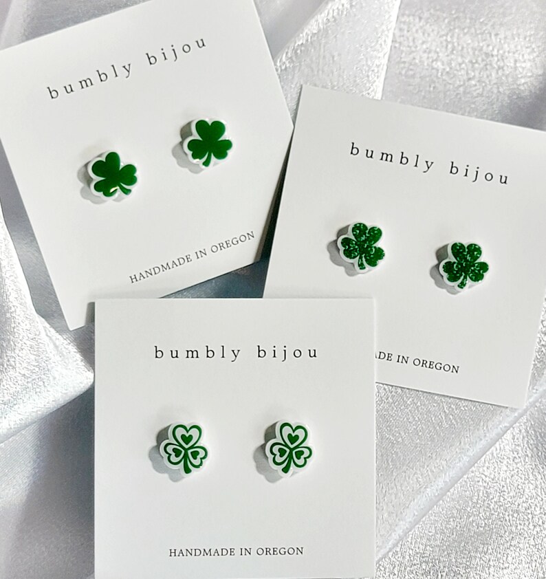 K&ouml;nnte beinhalten: Drei Paar gr&uuml;ne Kleeblatt-Ohrstecker auf wei&szlig;en Karten mit dem Text "bumbly bijou" und "handgefertigt in Oregon".