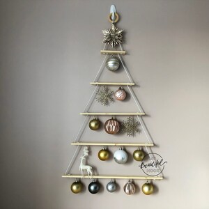 Könnte beinhalten: Ein hölzerner Weihnachtsbaum-Wandbehang mit einem Stern, Schneeflocken und Kugeln. Der Baum besteht aus vier Regalen und ist mit goldenen, silbernen und rosafarbenen Kugeln geschmückt. Der Text "My Beautiful Nook" steht auf dem untersten Regal.