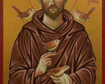 May include: A religious icon depicting Saint Francis of Assisi, a Catholic saint known for his love of animals. The icon features a detailed painting of Saint Francis in a brown robe, holding four small birds in his hands. The background is a gold color with a halo around Saint Francis's head. The icon is titled "O' agios Frakiskos" in Greek.