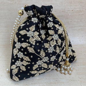 May include: Black drawstring pouch with gold floral embroidery and pearl accents. The pouch has a gold drawstring closure and a pearl tassel. The bag is made of a soft, velvety material, suitable for carrying small items.