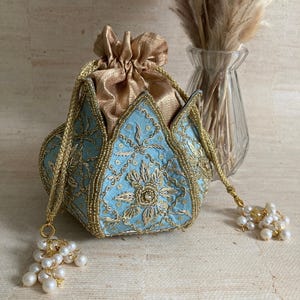 May include: A light blue, gold, and pearl beaded pouch with a drawstring closure. The pouch features intricate gold embroidery and pearl tassels. The interior is gold. A decorative item.