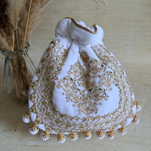 May include: White drawstring pouch with detailed gold embroidery, sequins, and pearl embellishments. The pouch has a gold trim and decorative gold tassels. A decorative item.