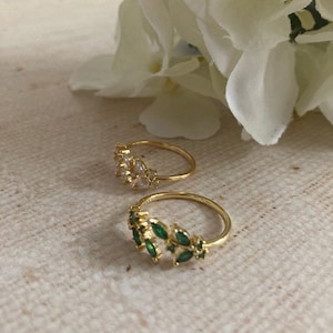 Könnte beinhalten: Zwei goldene Ringe mit grünen und klaren Steinen. Der Ring links hat klare Steine und der Ring rechts hat grüne Steine.