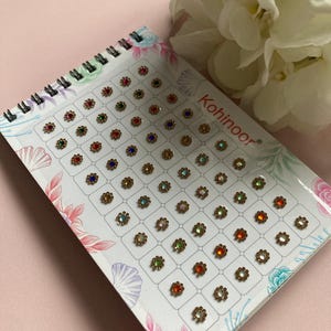 May include: A sheet of colourful, adhesive, flower-shaped rhinestones with a gold trim. The sheet is labelled "Kohinoor".