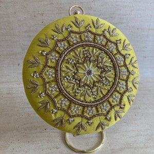 May include: A round, yellow clutch bag with a gold metal clasp and intricate beaded embroidery in a mandala design.