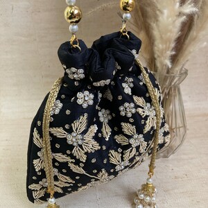 May include: Black drawstring bag with gold floral embroidery and pearl accents. The bag has a beaded handle with gold beads and a pearl tassel. A small, elegant accessory.