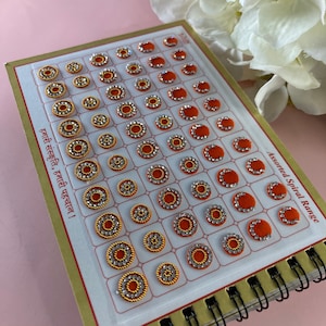 Könnte beinhalten: Eine Blatt mit verschiedenen spiralförmigen Bindi-Aufklebern mit weißem Hintergrund und goldfarbenem Rand. Das Blatt enthält 49 einzelne Bindis, jedes mit einer roten Basis und einem silbernen Spiralmuster. Der Text "Assorted Spiral Range" ist in der rechten unteren Ecke des Blattes gedruckt.