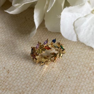 May include: A gold ring featuring a colourful, leaf-shaped design. The ring is set with small, multi-coloured gemstones.