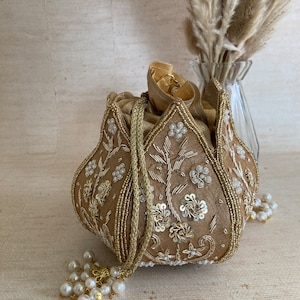 May include: A gold embroidered pouch with a floral design and pearl accents. The pouch has a drawstring closure and a tassel.