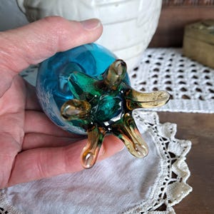 May include: A blue glass vase with a green and brown swirl design. The vase has a unique, spidery base with six legs.