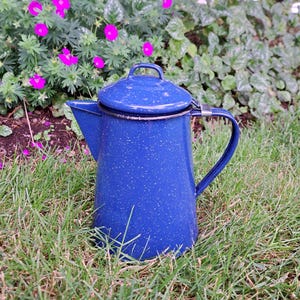May include: A cobalt blue enamel coffee pot with a speckled white pattern, featuring a matching lid with a small handle, a tapered body, a side spout, and a curved metal handle attached with a silver-toned metal band at the top rim.
