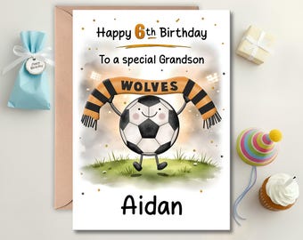 May include: A birthday card featuring a cartoon soccer ball wearing a black and orange scarf with "WOLVES" on it. The card says "Happy 6th Birthday To a special Grandson Aidan". Birthday gifts and a cupcake are also visible.